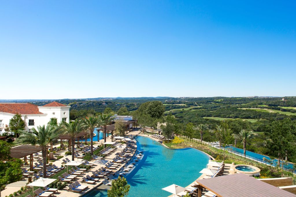 A swimming pool area in the center of the picture, pool benches to the left and the golf course in the bakground.